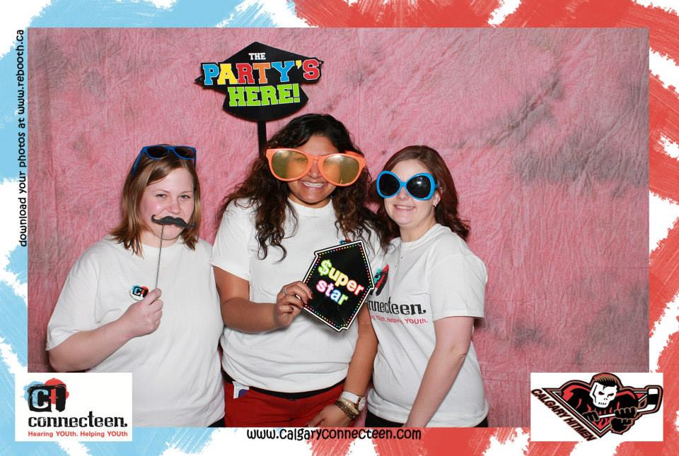 img des: Three people in a photobooth, using props like sunglasses and a fake mustache