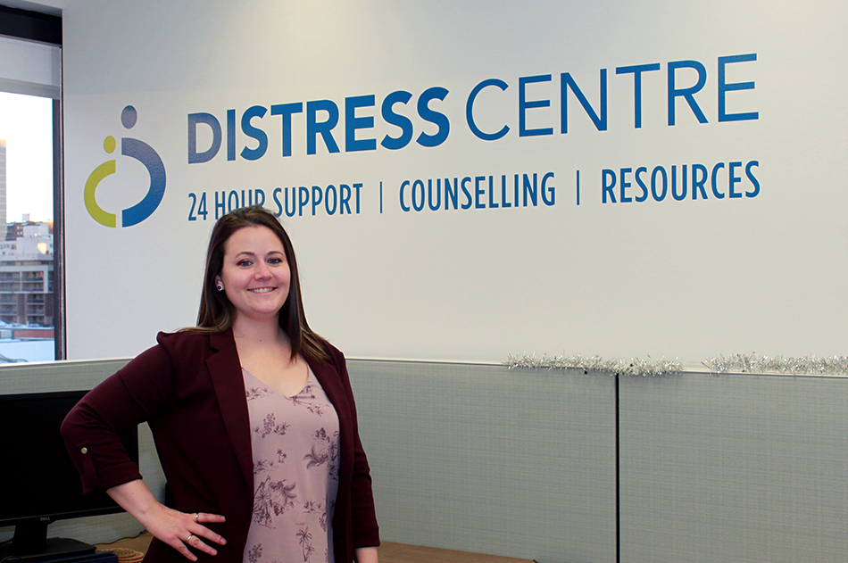 img des: Robyn Romano in the contact centre, standing in front of the DC logo on the wall.